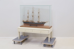 Modellskepp i glasmonter, glas/trä/textil, samt bord, 2 lådor, trä.