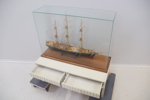 Modellskepp i glasmonter, glas/trä/textil, samt bord, 2 lådor, trä.
